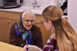 Elderly resident wearing a scarf speaks with a teenager from Temple Beth Am.