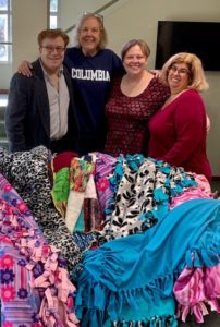 Three members of TBA staff stand with the regional Project Ezra coordinator behind colorful blankets that have been spread out over the sofa in the Temple lobby.